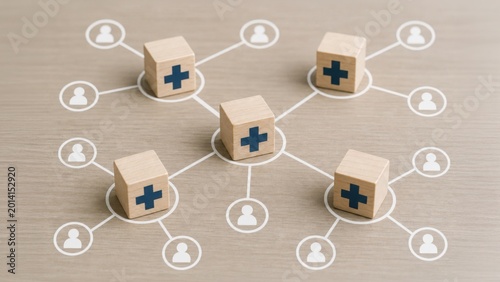 Wooden blocks with medical crosses form a network connecting to people icons, symbolizing a healthcare system, medical distribution, or health insurance network.