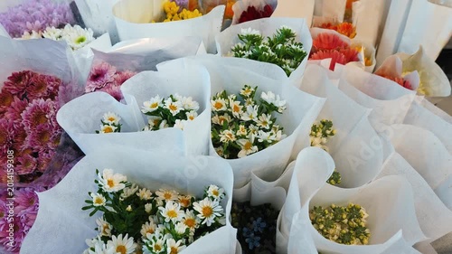 Mixed floral arrangements including Chrysanthemum and Bellis perennis in white paper wrap, flower market display, small business retail and floristry background, slow motion