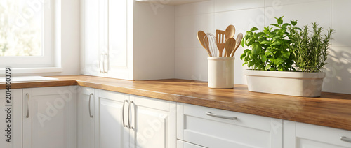 Modern white kitchen cabinet corner with wooden countertop featuring green herbs and wooden cooking utensils in natural sunlight