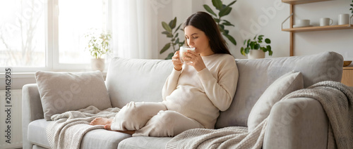 Pregnant woman relaxing on a sofa at home while drinking tea in a cozy indoor setting