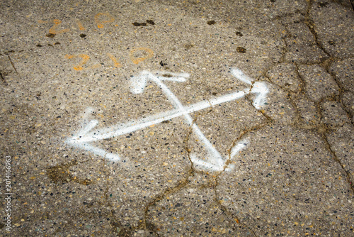Multl-direction chalk arrows on pavement, cracks in the surface, potholes and concrete for repair.