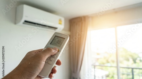 Close up of a hand holding a white remote control pointing at a wall mounted AC unit