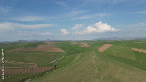 Rolling green hills and fields under a vast sky with white clouds.