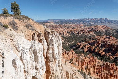 Foto Bryce Canyon white limestone cliffs overlooking orange hoodoo formations and vast desert valleys beneath a clear blue sky in Utah’s dramatic canyon landscape