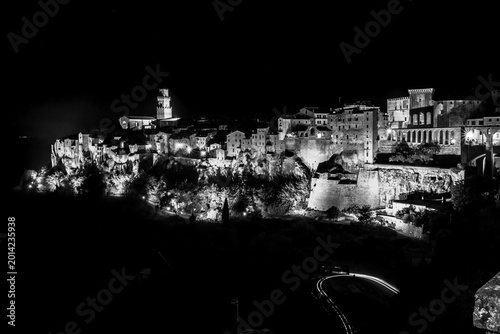 Black and white view of city at night with clock tower, Sovana, Tuscany, Italy, long exposure motion blur, car trails