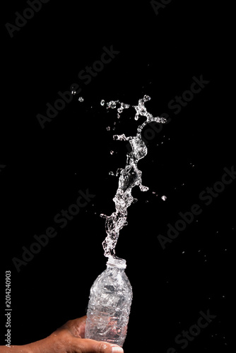 Fotografie Splashing water erupting from the top of the bottle against a dark background, c