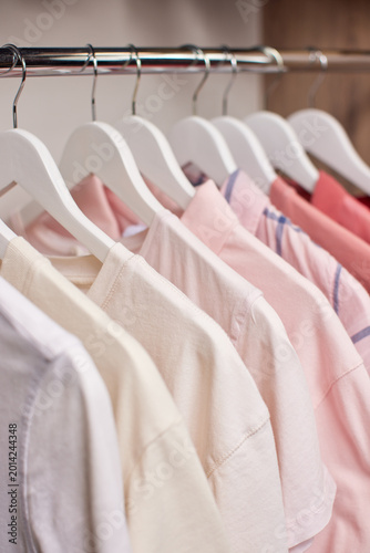 Clothing rail of neatly arranged pastel pink ombre t-shirts on white hangers, minimalist wardrobe display for boutique or closet photography