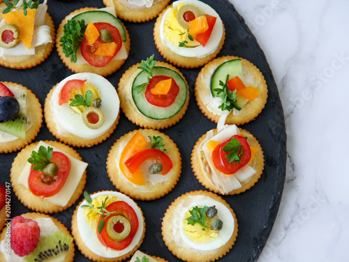 Flat lay overhead of colorful appetizers on dark stone serving dish placed on a marble counter for a party gathering. 