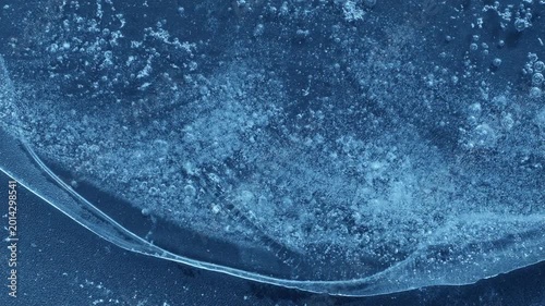 Extreme macro close-up of cracked blue melting ice texture in time lapse. Abstract frozen water surface with translucent crystal patterns, condensation and thawing details in studio lighting.
