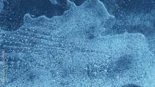Extreme macro close-up of cracked blue melting ice texture in time lapse. Abstract frozen water surface with translucent crystal patterns, condensation and thawing details in studio lighting.