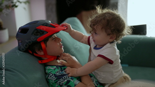 Obraz na płótnie Toddler lifting sibling’s helmet with playful curiosity while leaning close on c