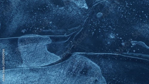 Extreme macro close-up of cracked blue melting ice texture in time lapse. Abstract frozen water surface with translucent crystal patterns, condensation and thawing details in studio lighting.