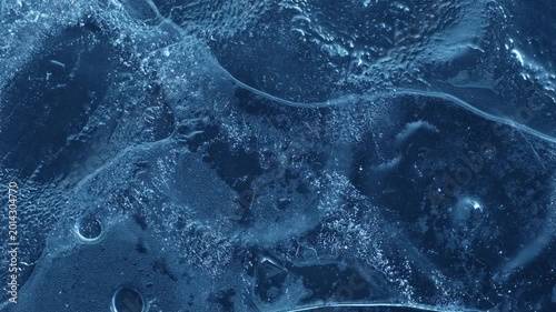Extreme macro close-up of cracked blue melting ice texture in time lapse. Abstract frozen water surface with translucent crystal patterns, condensation and thawing details in studio lighting.