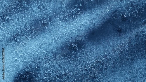 Extreme macro close-up of cracked blue melting ice texture in time lapse. Abstract frozen water surface with translucent crystal patterns, condensation and thawing details in studio lighting.