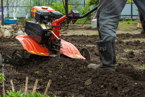 Tableau sur toile Farmer in rubber boots tilling garden soil with gasoline cultivator