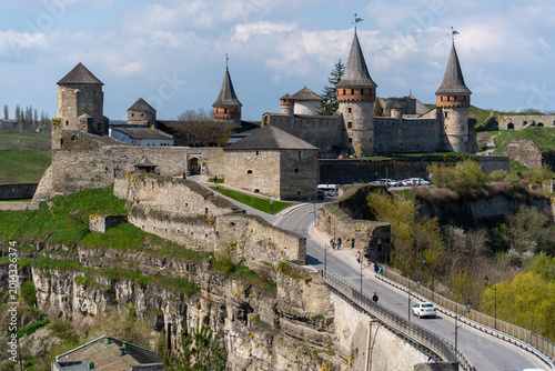 View of Kamianets-Podilskyi Castle with its stone towers and fortified walls overlooking a rocky gorge and a bridge with people walking Kamianets-podilskyi, Khmelnytska oblast, Ukraine.