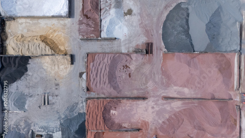 Top down aerial view of different piles of sand, gravel and raw construction materials stored in an industrial yard. Abstract patterns, textures and colors created by mineral aggregates from above.