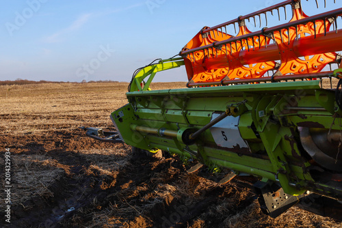 Valokuva ​A powerful green combine harvester header is stuck in deep mud in the middle of a mown field