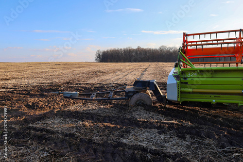 Slika na platnu An agricultural trailer with a combine harvester header is stuck deep in wet soil in the middle of a mown field under a clear sky