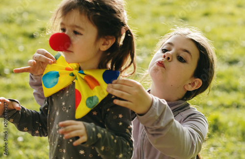 Slika na platnu Portrait of two girls dressing up as clowns in a park.