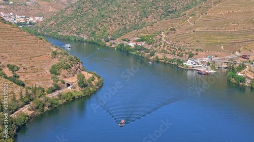 Douro river boat near vineyard village in Portugal daylight, with blue water, terraced banks, riverside buildings and wine hills.