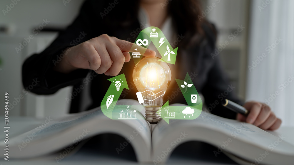 Naklejka premium Spark of Innovation: A Business Person Holding a Light Bulb Over an Open Book with Eco-Friendly Icons Representing Sustainability and Energy Solutions Quark.