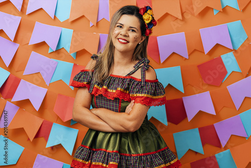Brazilian woman wearing typical clothes for the Festa Junina dancing on colorful background with pennants