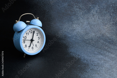 Fotografie Bright blue alarm clock resting on a dark textured surface while time ticks away