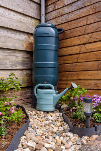 Rain barrel with gravel path and a blue watering can in garden