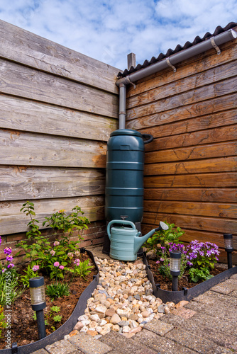 Rain barrel with gravel path and a blue watering can in garden