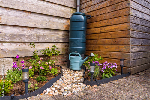 Rain barrel with gravel path and a blue watering can in garden