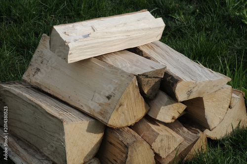 Firewood stacked in a pile on the green grass, close up.