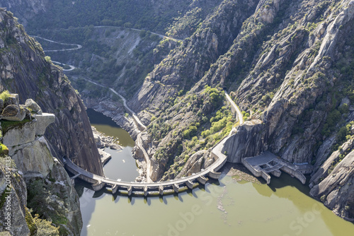 View of the Aldeadavila Dam and its curved wall nestled between steep granite cliffs and winding roads in the Duero River canyon Aldeadavila de la Ribera, Castile and Leon, Spain.
