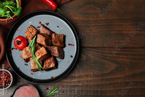 Pieces of delicious beef meat with spices, sauce and tomato on wooden table, flat lay. Space for text