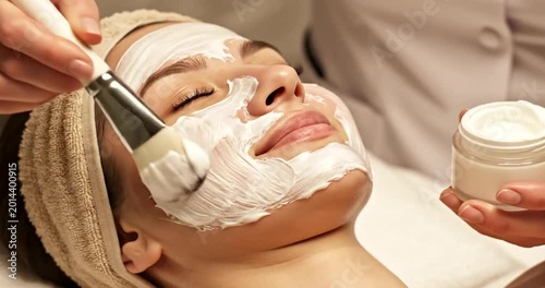 Professional spa treatment with facial mask application and skincare product jar close-up