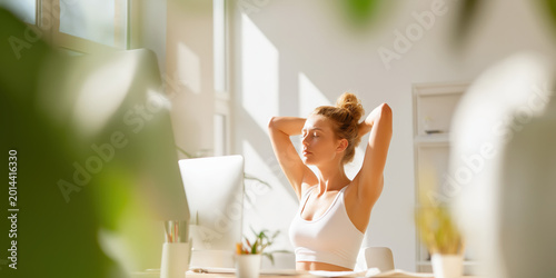 Young woman stretching at her desk in a bright sunny home office