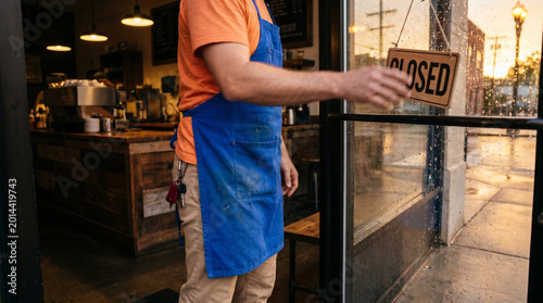 Barista closing the coffee shop early while hanging a closed sign  