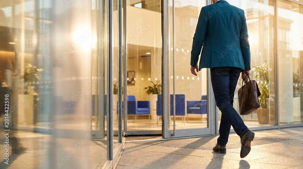 Fototapeta premium Office worker leaving building with briefcase during sunset 