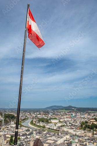 View the city of Salzburg from a high point. The Austrian flag stands tall against the sky.