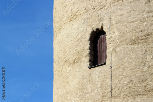 Small arched wooden window in ancient stone tower wall