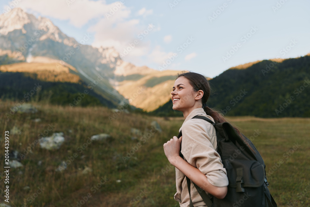 Naklejka premium An outdoor woman with a backpack stands in a mountain valley, smiling into the distance. A lifestyle portrait capturing hiking, travel, and nature curiosity.