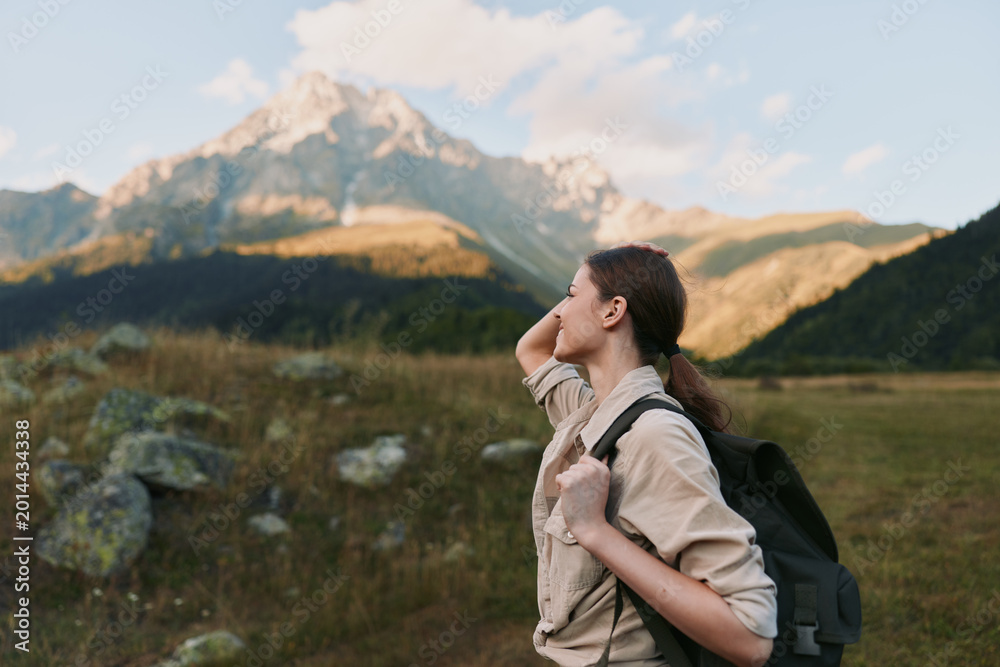 Naklejka premium Woman hiker with backpack admires distant alpine peaks in a wide meadow, enjoying a calm outdoor lifestyle moment and fresh mountain air. She explores rugged scenery.