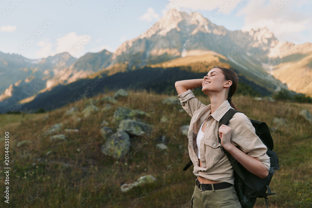 Fototapeta premium Cheerful woman hiking outdoors, backpack on, sunlit mountain landscape, relaxed posture, gentle breeze, vivid wildflowers, natural colors, vast scenery, wide sky above