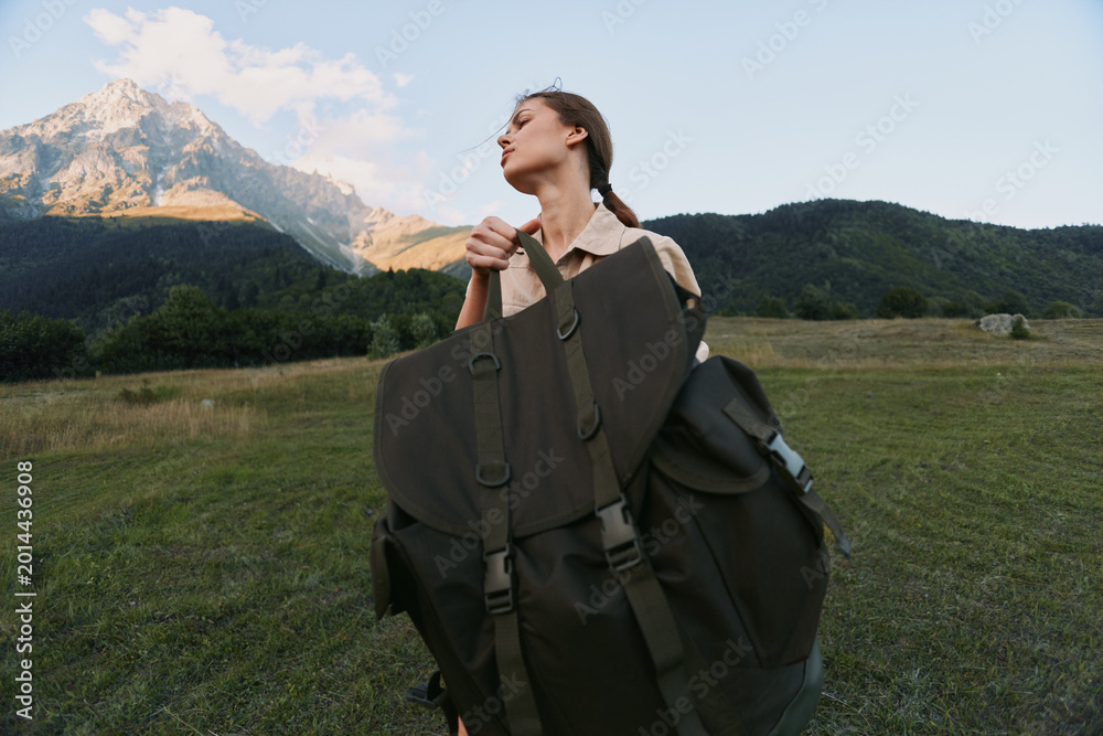 Fototapeta premium A young woman hiker with a large backpack stands in a wide meadow, mountains in the background, conveying determination, anticipation, and a spirit of adventure.