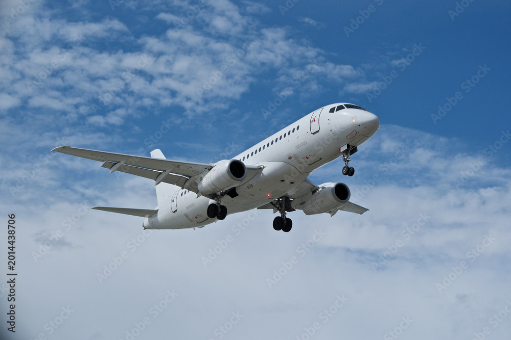 Obraz premium White Airplane Approaching for Landing Against Blue Sky with Clouds