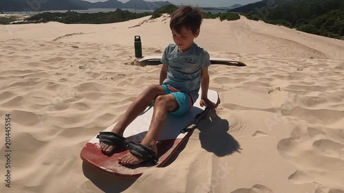 Young boy getting ready to slide down sand dunes on board in South America