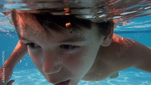 Young boy swimming in outdoor pool in tropical location looking towards camera as his head is underwater