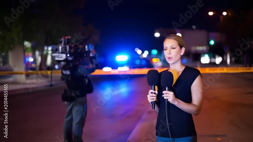 Female news reporter broadcasting from police scene, live journalism coverage, television camera crew, breaking news, crime scene tape, emergency lights and public safety report