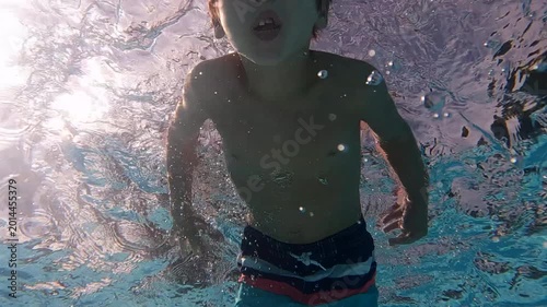Young happy boy swimming in outdoor pool in summer - smiling underwater