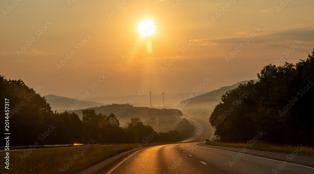 Fototapeta premium Highway Through Misty Mountain Landscape at Sunrise with Golden Light Fog and Rolling Hills Creating Atmospheric Scenic View